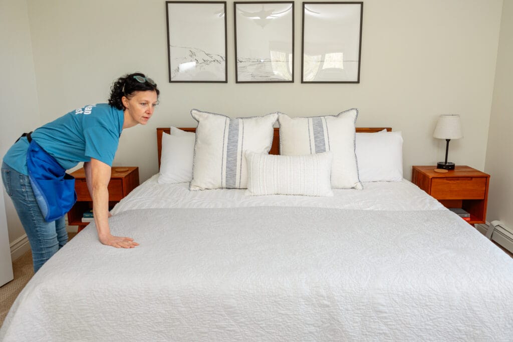 OrchardCleaningTraverseCityMichiganCapturedByGraceHudsonPhotography2024-125 Orchard cleaning technician smoothing a freshly made bed during a recurring house cleaning visit